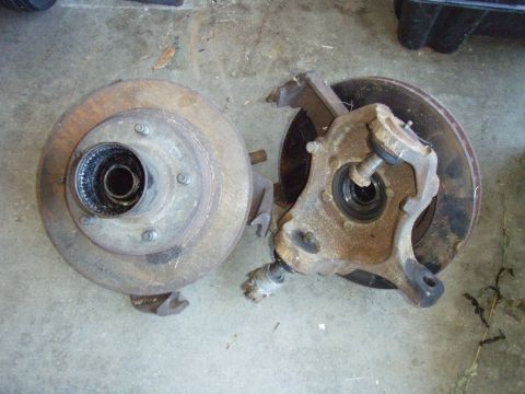 1994 Ford Bronco - Disassembled vehicle brake components, including a rotor and spindle, are shown on a garage floor.