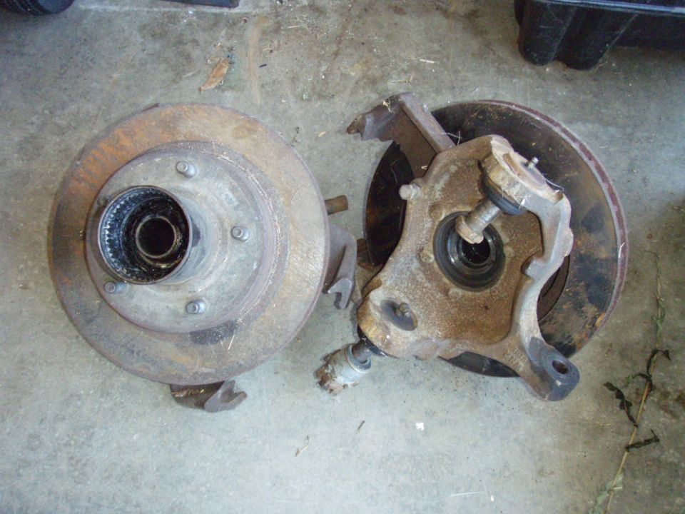 Brake rotor and spindle assembly with visible rust and wear, lying on a concrete floor