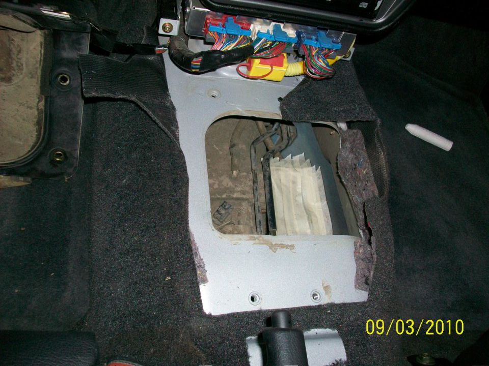 Car interior with exposed wiring and metal paneling. A white chalk-like object rests on black carpet