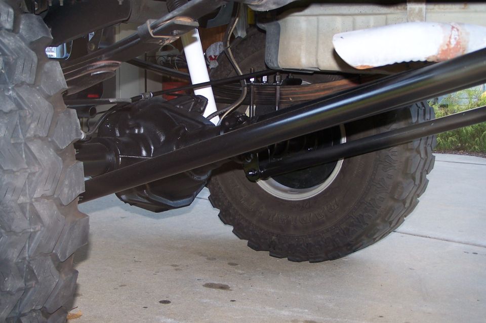 Close-up of a vehicle's rear axle, leaf springs, and large tire. Black painted components and a white shock absorber are visible