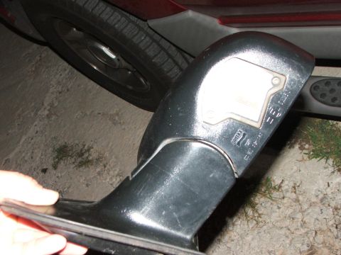 2003 Ford Sport Trac - A detached side mirror assembly from a red 2003 Ford Sport Trac is held by a hand, revealing text on the housing.