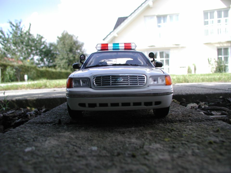 White police car with red and blue light bar, front view, parked on a concrete surface