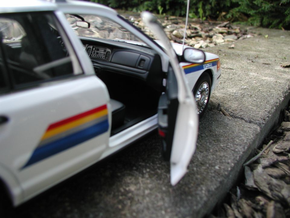 White diecast RCMP police car model with door open on concrete steps