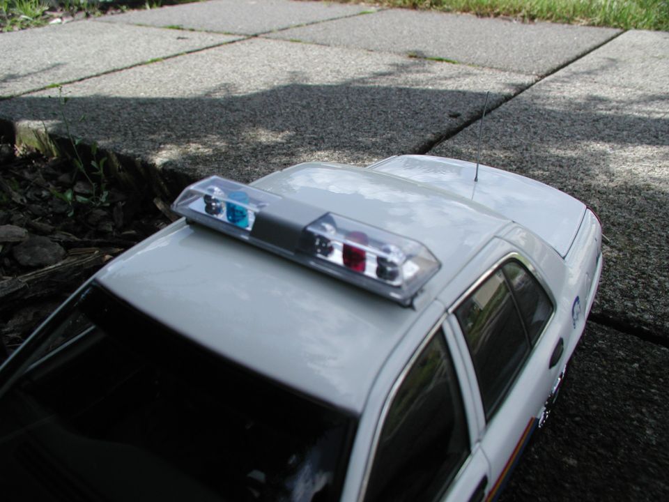 White diecast model police sedan with roof lightbar on a sidewalk