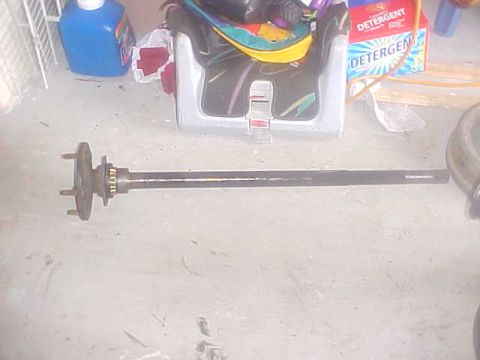 1996 Ford Bronco - An axle shaft is shown lying on a floor with laundry detergent boxes and a car seat in the background.