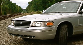 2000 Ford Crown Victoria - A silver 2000 Ford Crown Victoria is parked next to railroad tracks under a cloudy sky.