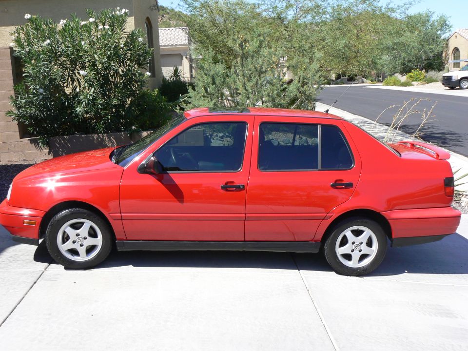 Red sedan parked on a concrete driveway with trees and a house in the background