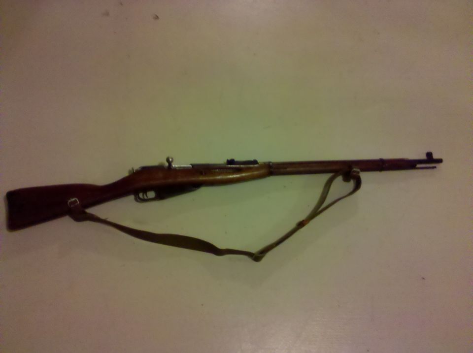Wood-stocked bolt-action rifle with leather sling laid on a plain surface