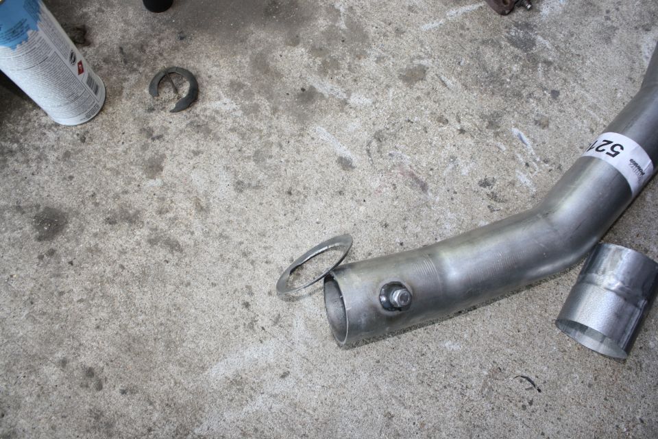 Exhaust pipe sections and a clamp on a concrete floor. A can of spray is also visible