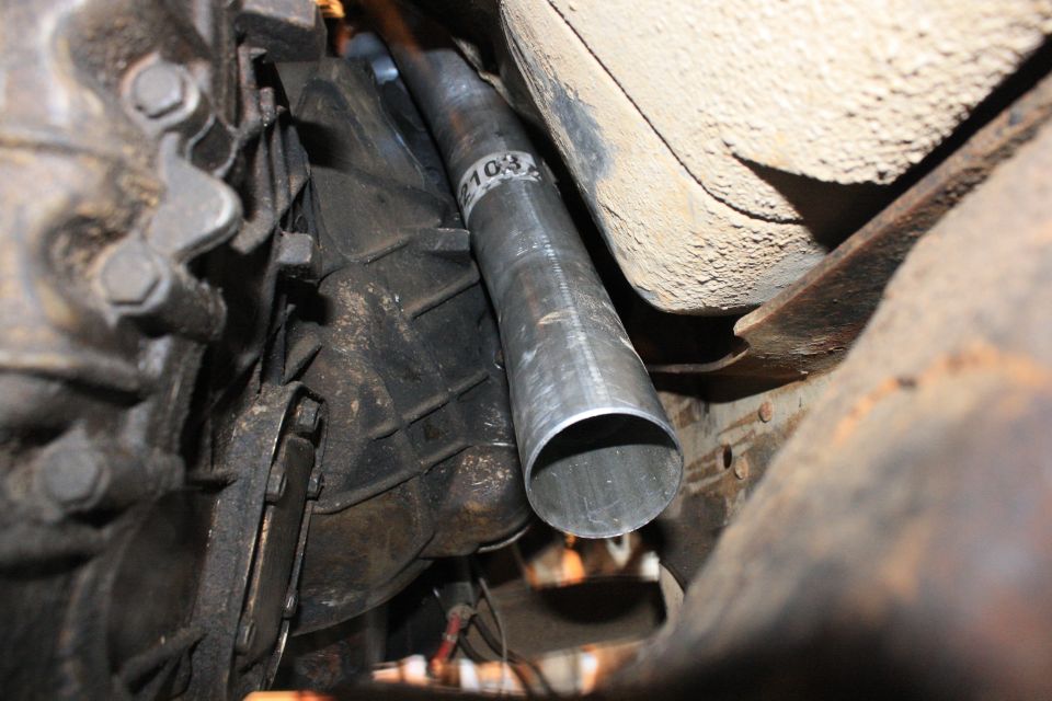 Close-up of a vehicle's transmission and a new exhaust pipe section with a "103" marking