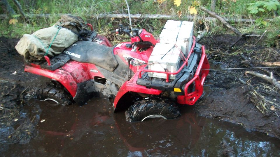 Red Polaris all-terrain vehicle stuck in mud, with gear strapped to the rear rack