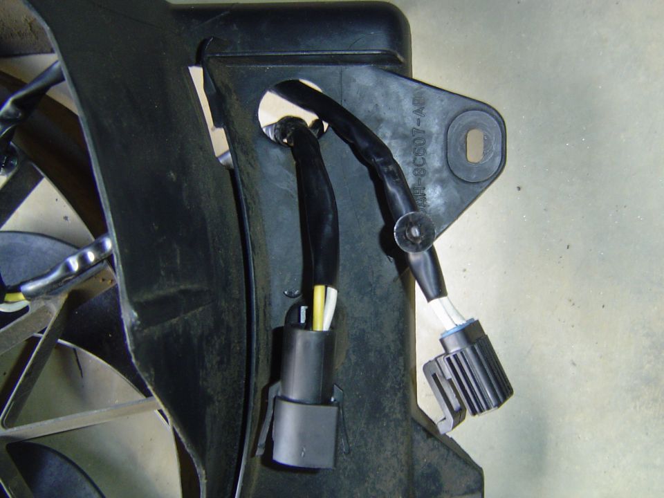Close-up of a radiator fan shroud with wiring harnesses and connectors. Part number visible on shroud