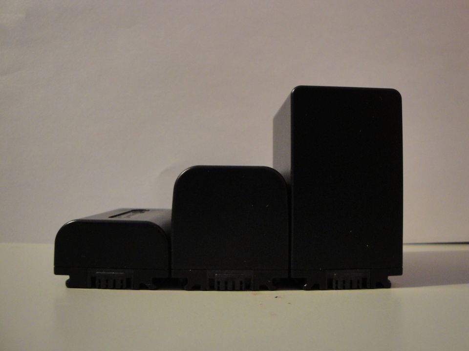 Three black camera batteries lined up on a white surface, viewed from the side