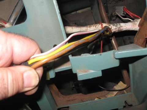 1981 Ford Bronco - Close-up of a hand holding a bundle of wires near the dashboard of a vehicle.