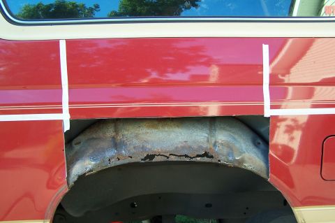 1990 Ford Bronco - The wheel well of a red SUV shows significant rust damage, with white tape marking the area.