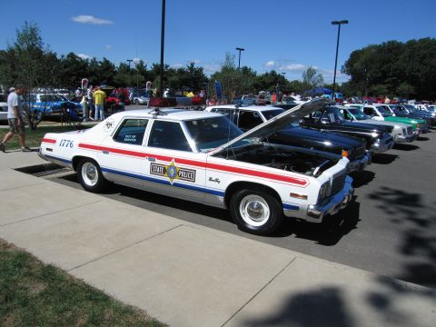 1991 Ford LTD Crown Victoria - white STATE POLICE sedan marked #1776 with red-and-blue stripes and an open hood sits in a row of show vehicles.