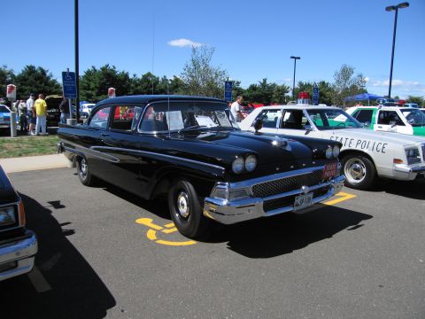 1991 Ford LTD Crown Victoria - black late-1950s-style two-door sedan with quad headlights sits beside white STATE POLICE cars at an outdoor show.