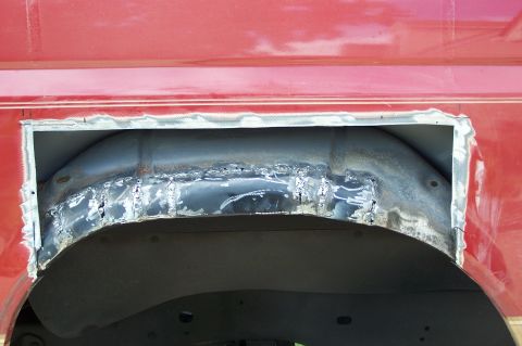 1990 Ford Bronco - Modification to the rear wheel well of a red vehicle, showing cut metal and welding marks.