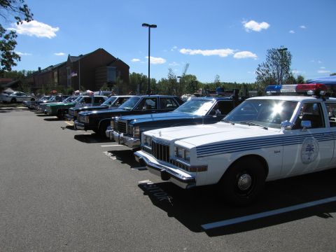 1991 Ford LTD Crown Victoria - row of vintage police cars lined up at an outdoor show, led by a white Dodge Diplomat with blue stripes.