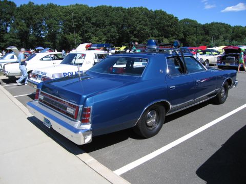 1991 Ford LTD Crown Victoria - Rear quarter view of a blue 1970s Ford LTD police sedan with roof spotlight and siren among show cars.