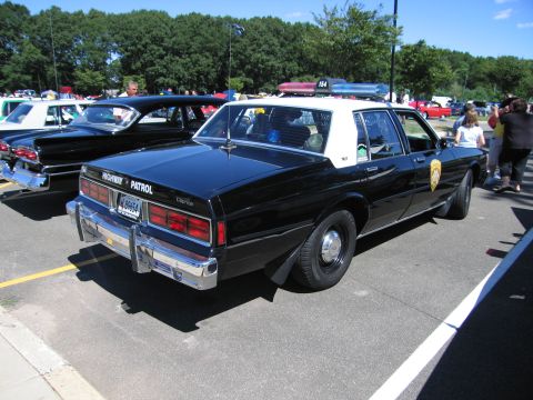 1991 Ford LTD Crown Victoria - Rear quarter view of a black-and-white Highway Patrol Chevrolet sedan with roof light bar at a car show.