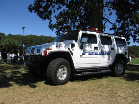 1991 Ford LTD Crown Victoria - white Hummer H2 marked POLICE serving as a DUI enforcement vehicle, parked on grass under a tree.