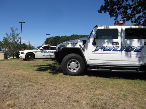 1991 Ford LTD Crown Victoria - white POLICE Hummer H2 parked on grass next to a white Dodge Charger traffic-enforcement cruiser.