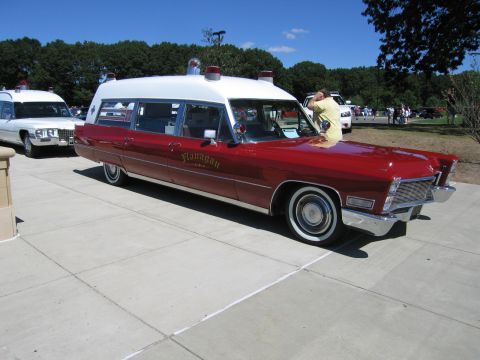 1991 Ford LTD Crown Victoria - red-and-white vintage Cadillac ambulance lettered Flanagan parked on pavement at an outdoor car show.