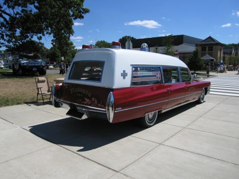 1991 Ford LTD Crown Victoria - red and white classic Cadillac ambulance with roof lights and 'Ambulance' lettering parked on pavement at a sunny car show.
