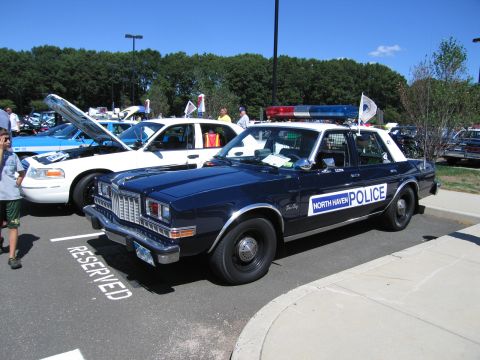 1991 Ford LTD Crown Victoria - dark blue four-door 'North Haven Police' sedan with roof light bar parked in a reserved spot among show cars on a sunny day.