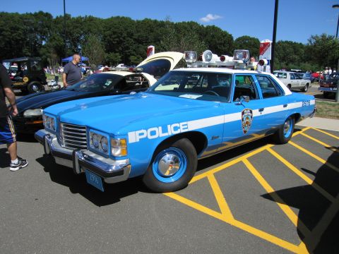 1991 Ford LTD Crown Victoria - light blue vintage four-door 'Police' sedan with NYPD-style markings and roof beacons parked in a striped lot at a show.
