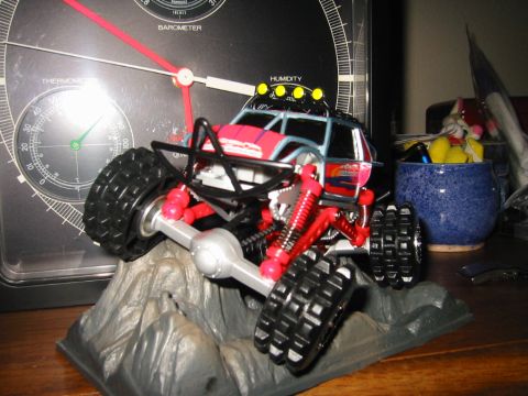 1985 Ford Bronco - This remote control rock crawler toy features bright red suspension components and off-road tires, displayed on a rocky base.