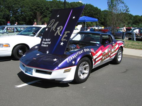 1991 Ford LTD Crown Victoria - Chevrolet Corvette painted in purple, white and red stars-and-stripes 'D.A.R.E. Connecticut State Police' livery with hood raised.