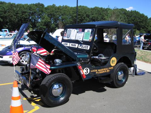 1991 Ford LTD Crown Victoria - dark green flat-fender Jeep lettered 'Look Park Police, Look Memorial Park, Florence MA' with hood open and American flags, at a show.