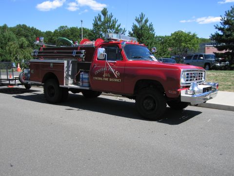 1991 Ford LTD Crown Victoria - red 4x4 fire engine lettered 'Central Fire Co, Central Fire District' with chrome bumper and hose reel, parked on a road at a show.
