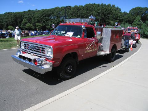 1991 Ford LTD Crown Victoria - red 4x4 fire engine marked 'Central Fire District' with chrome front bumper and roof beacons, parked on a road with show cars behind.