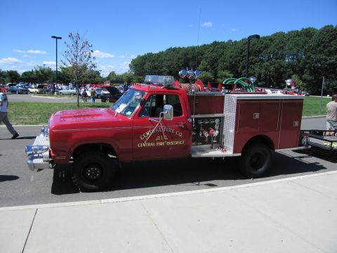 1991 Ford LTD Crown Victoria - red 4x4 fire engine lettered 'Central Fire Co, Central Fire District' with hoses and equipment box, parked on pavement at a car show.