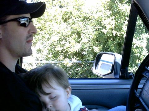 1995 Ford Bronco - Man and sleeping child inside a 1995 Ford Bronco, with trees visible through the window.