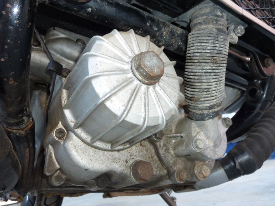 Finned aluminum cover with large hex bolt on a grimy motorcycle engine case