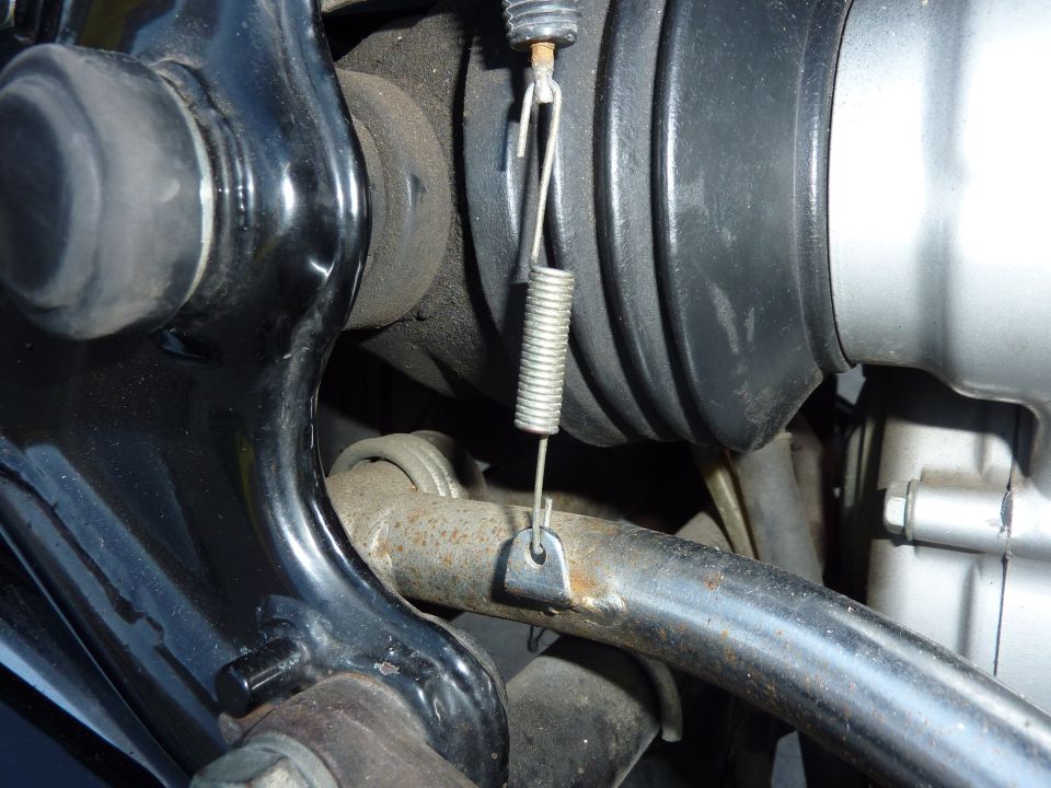 Return spring hooked to a bracket beside a motorcycle driveshaft boot and final drive