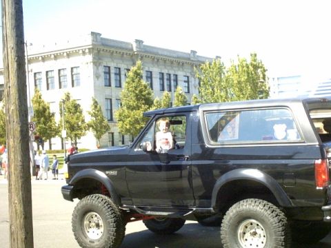 1995 Ford Bronco - A child sits in the driver's seat of a lifted black Ford Bronco parked on a street.