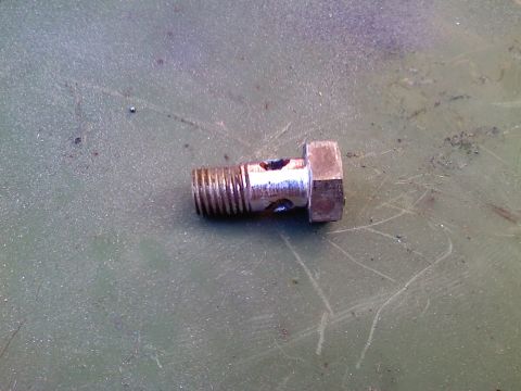 1990 Ford Bronco - A banjo bolt, a type of fastener used in hydraulic systems, is shown on a green surface.