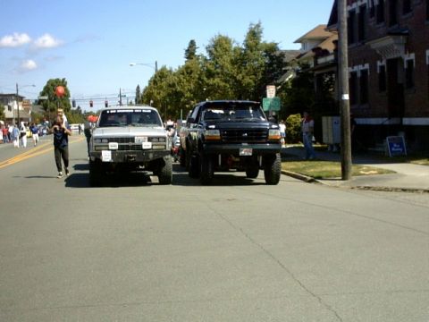 1995 Ford Bronco - Two lifted trucks, a black Ford and a silver truck, are parked side-by-side on a street.