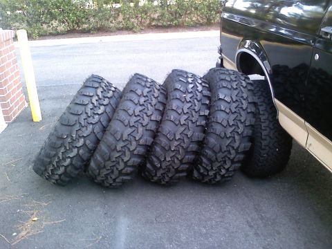 1990 Ford Bronco - A set of aggressive off-road tires are lined up next to a vehicle's rear fender and door.