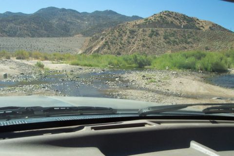 1995 Ford Bronco - Driving through a dry riverbed with mountains in the background. Supermotors.net logo is visible.