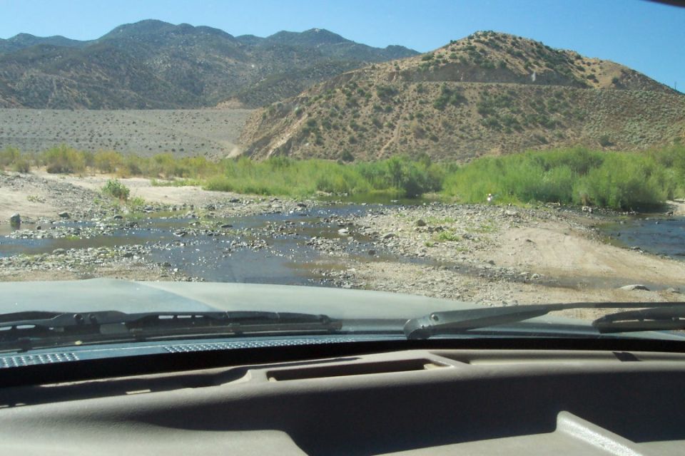 View from inside a vehicle looking out at a dry riverbed and mountains. Supermotors.net logo visible