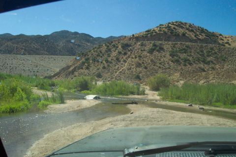 1995 Ford Bronco - A 1995 Ford Bronco navigates a shallow riverbed surrounded by arid hills and green brush.