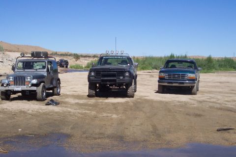 1995 Ford Bronco - Three SUVs and trucks are parked on a dirt path under a clear blue sky.
