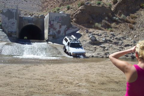 1995 Ford Bronco - A white SUV navigates through a water crossing in a dry, rocky landscape.