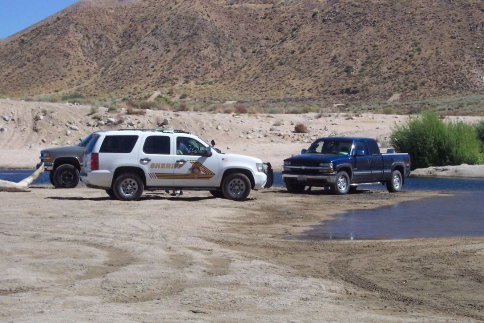 White sheriff SUV and two pickup trucks in a dry riverbed